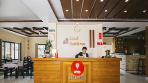 Una recepción de hotel con una recepcionista, un reloj y un cartel que indica Hotel Sublime.