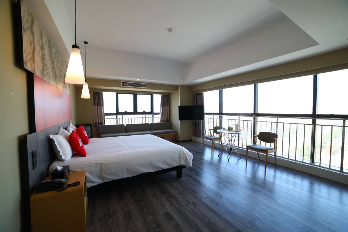 A spacious hotel room with a large bed, a seating area with a view, and a balcony.