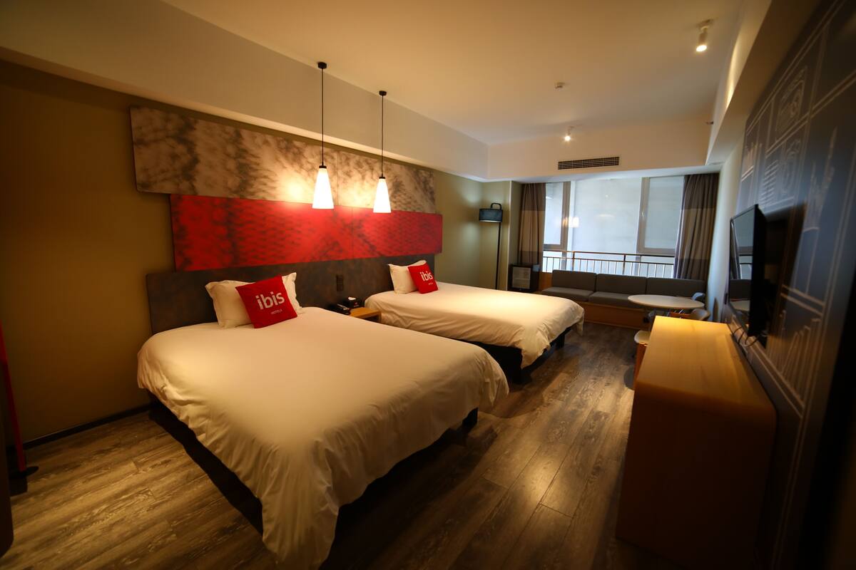 A hotel room with two beds, a large window, a TV, and a wooden floor.