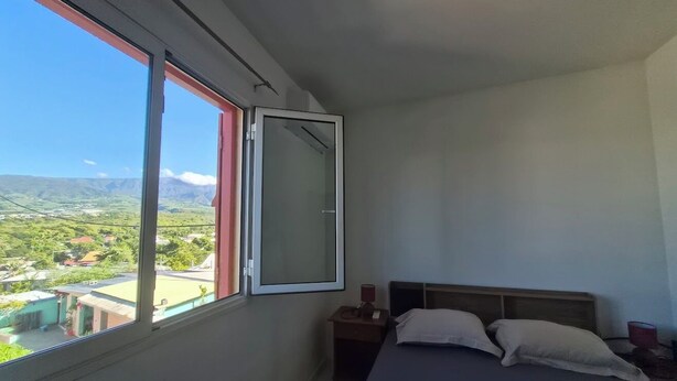 Une chambre à coucher avec un lit, une table de chevet, une lampe et une fenêtre donnant sur un paysage.