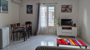 Un salon comprenant une table à manger, des chaises, un téléviseur posé sur un meuble, un ventilateur de plafond et une porte-fenêtre donnant sur un balcon.