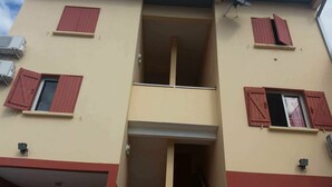 Un immeuble à plusieurs étages avec des volets rouges aux fenêtres, un balcon bien visible et des unités de climatisation.