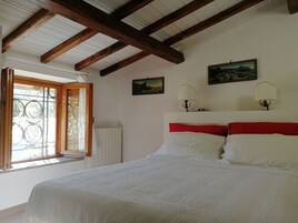 Un dormitorio con techo de madera, una cama con ropa de cama blanca y roja, dos lámparas de pared y dos cuadros enmarcados.