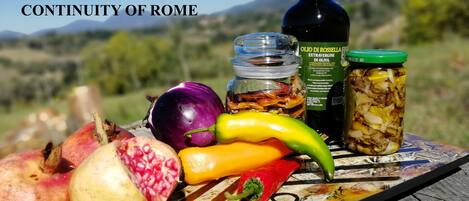 A table with various food items and a bottle of olive oil in an outdoor setting.
