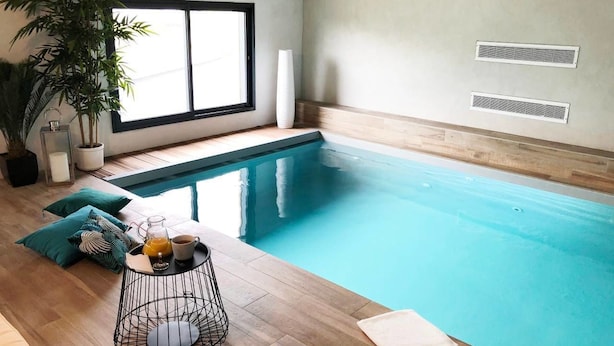 An indoor swimming pool with a wooden floor, a table with a drink, and a potted plant. - Il Etait Une Fois à L'Ouest (Plestan)