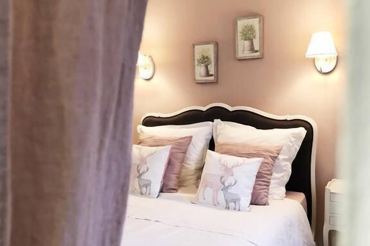 A bedroom with a bed, pillows, wall-mounted lights, and framed pictures.