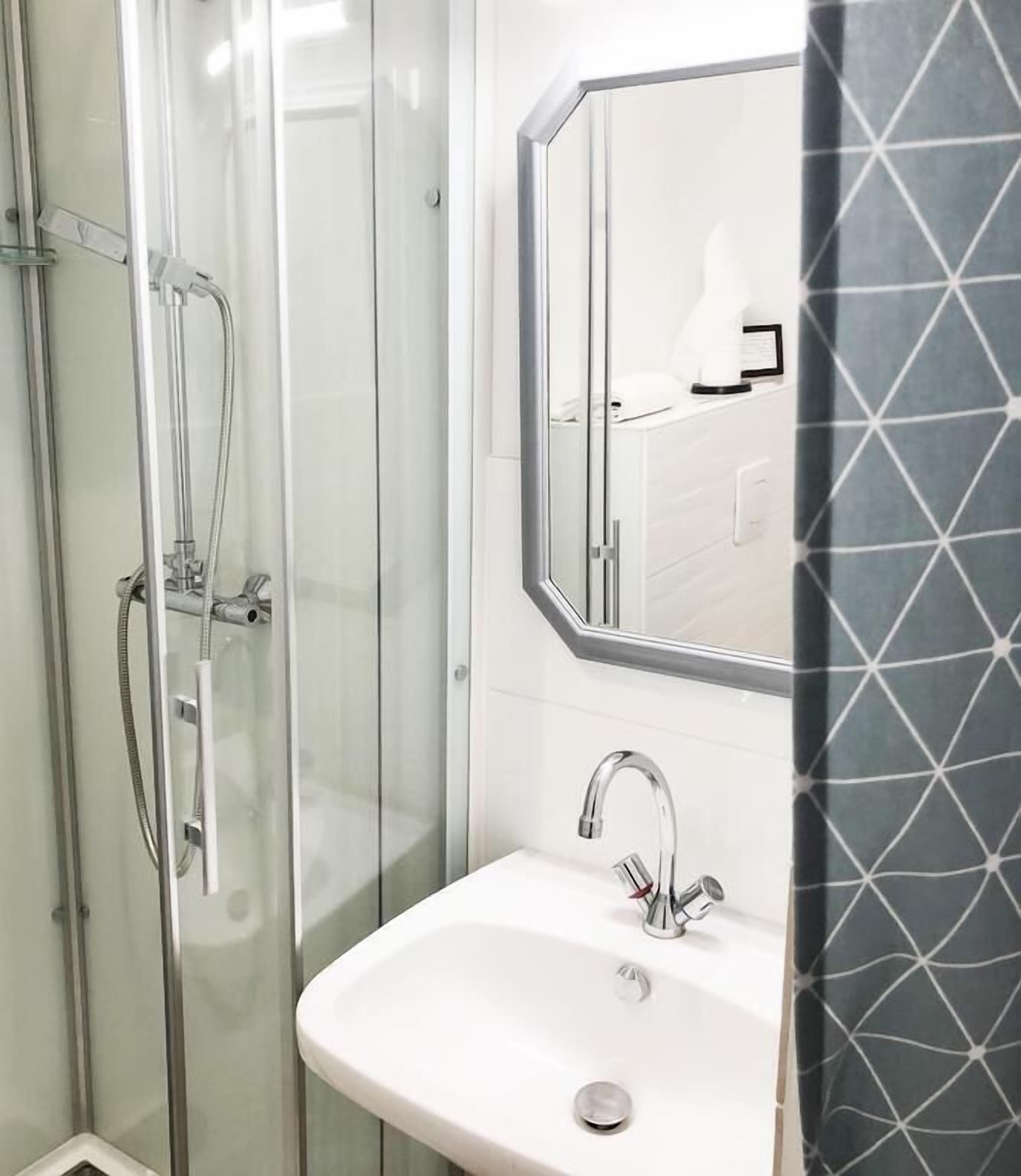 A modern bathroom with a glass shower enclosure, a white sink, and a large mirror.
