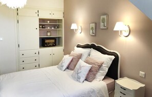 A bedroom with a bed, bedside tables, a wardrobe, wall-mounted lamps, and a shelf with decorative items.