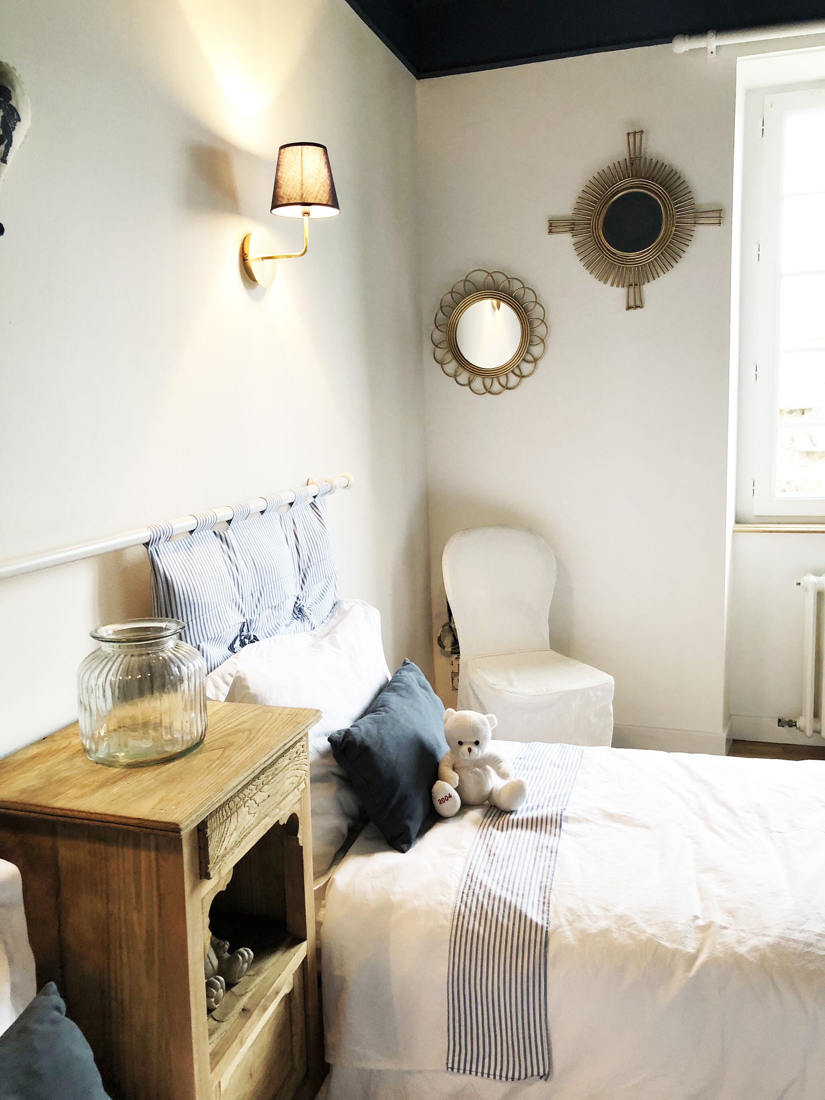 Un dormitorio con cama, mesita de noche, lámpara y espejos decorativos.