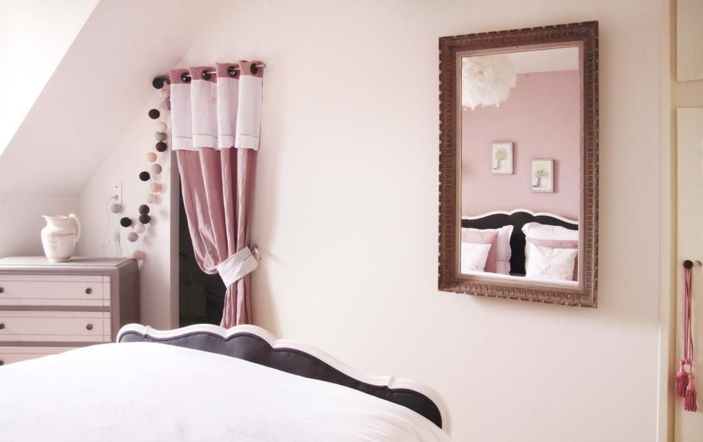 A bedroom with a bed, a dresser, a mirror, and a wall with a picture frame.