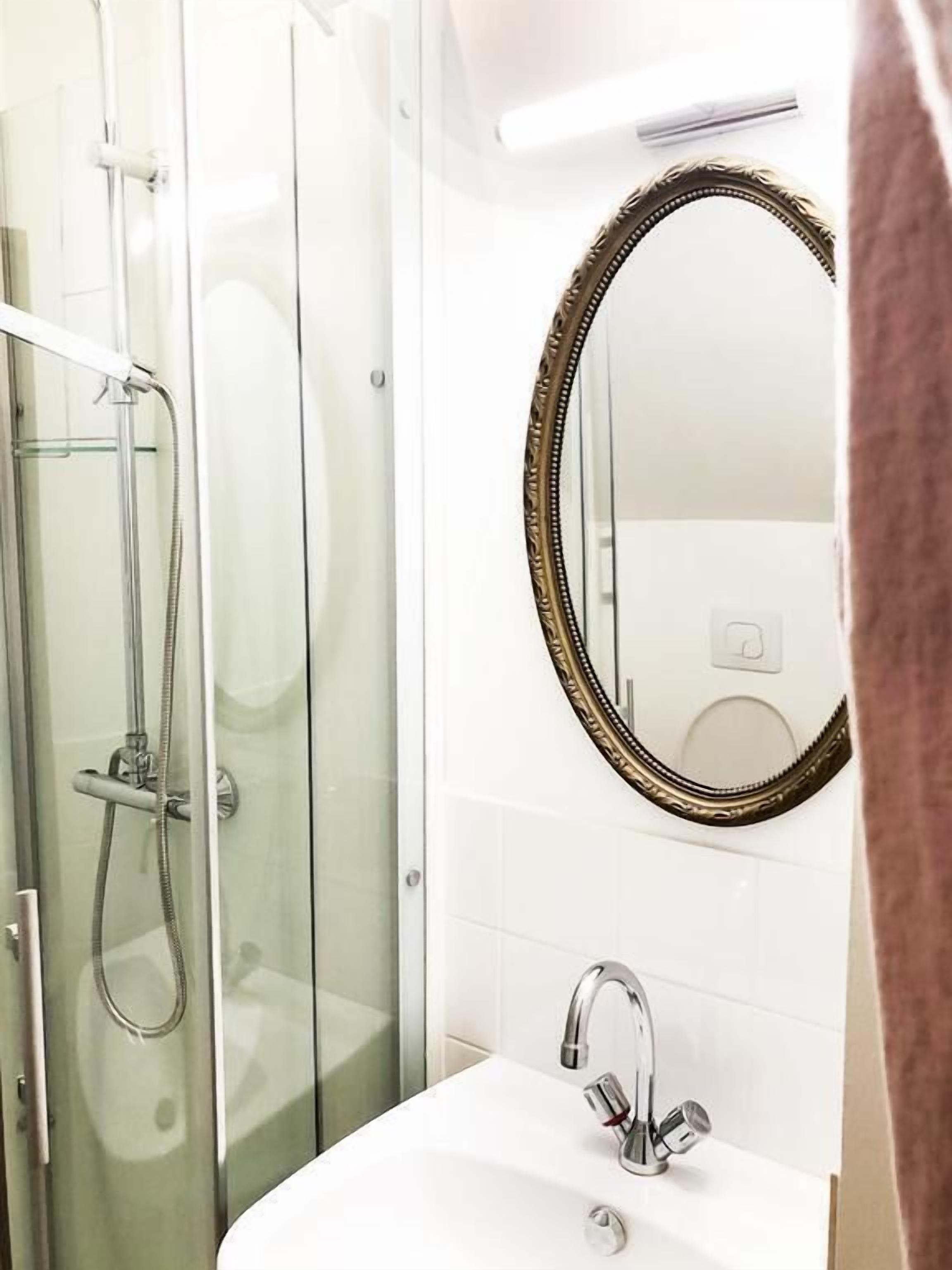 Un baño con ducha de vidrio, un lavamanos blanco con grifo moderno y un espejo grande con marco decorativo.