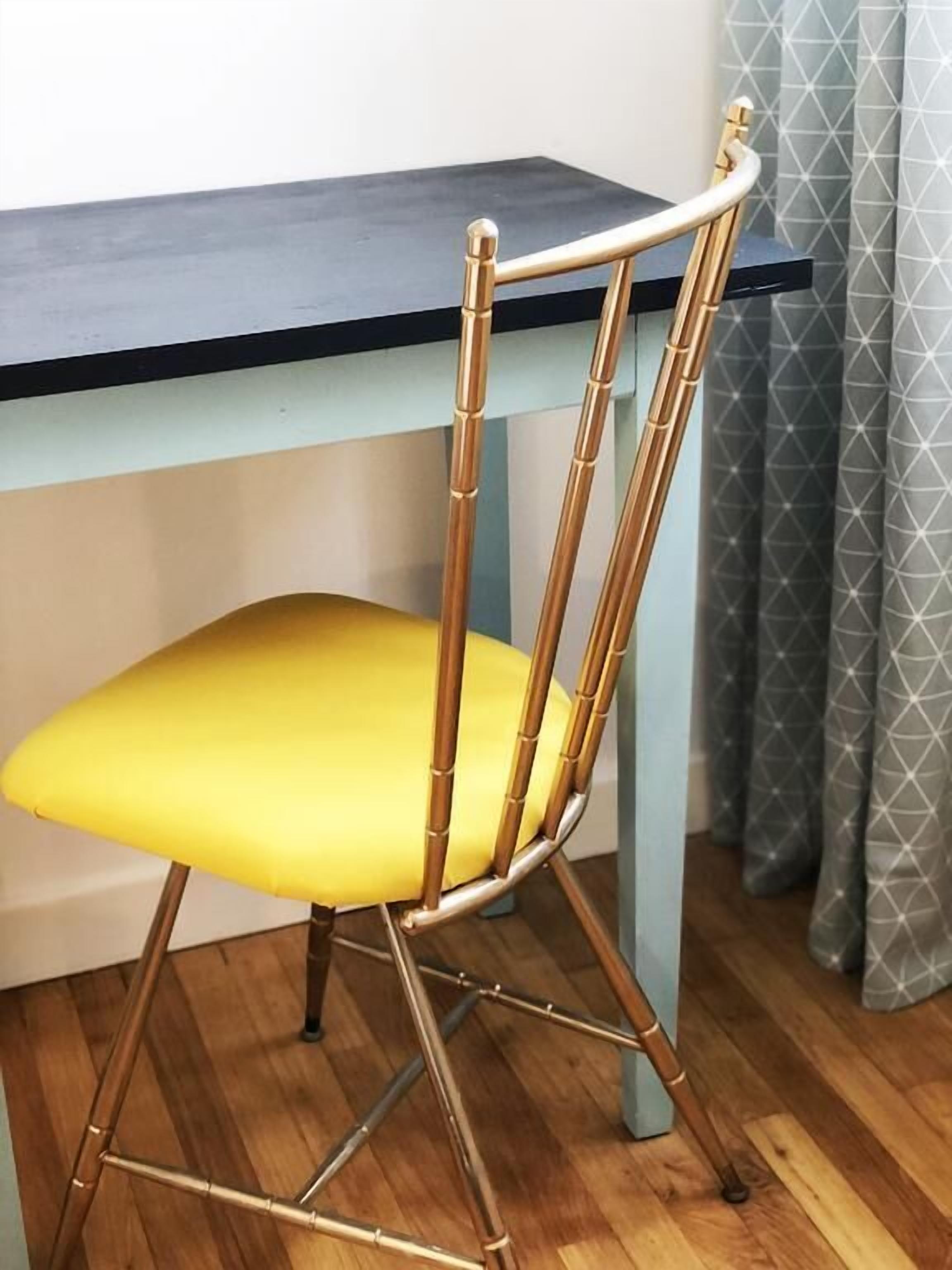 Una silla con un cojín amarillo y estructura de bambú, ubicada frente a una mesa oscura.