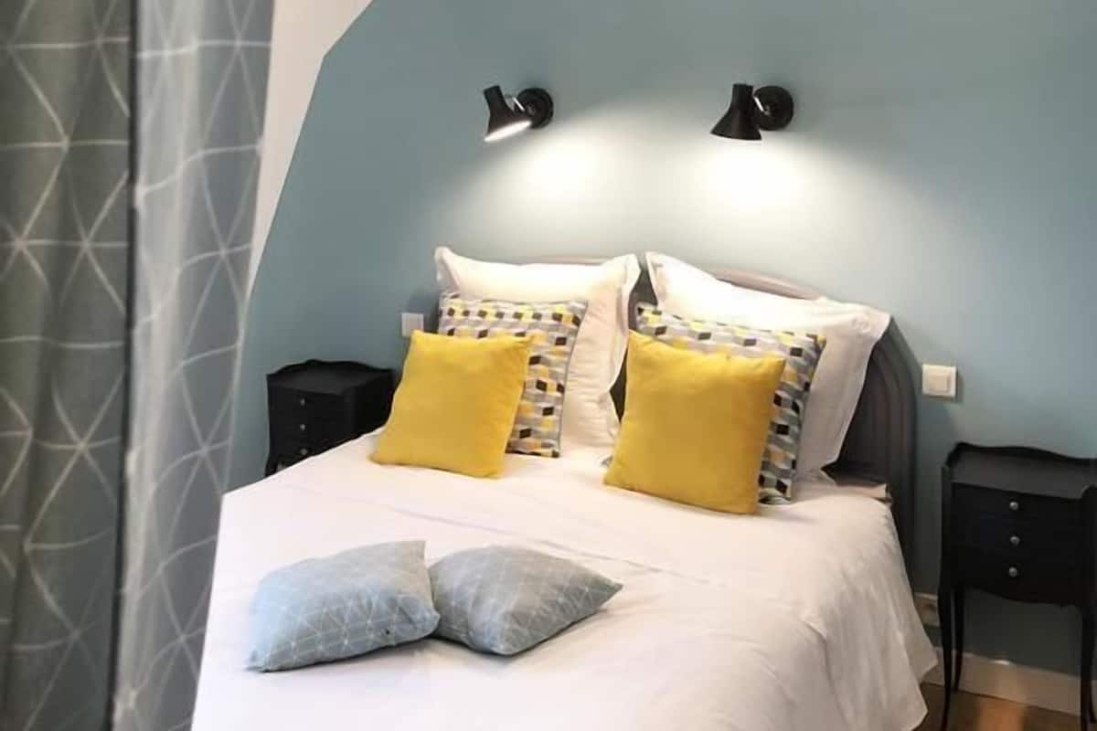 A bedroom with a bed, two bedside tables, a nightstand, a lamp, and a curtain.