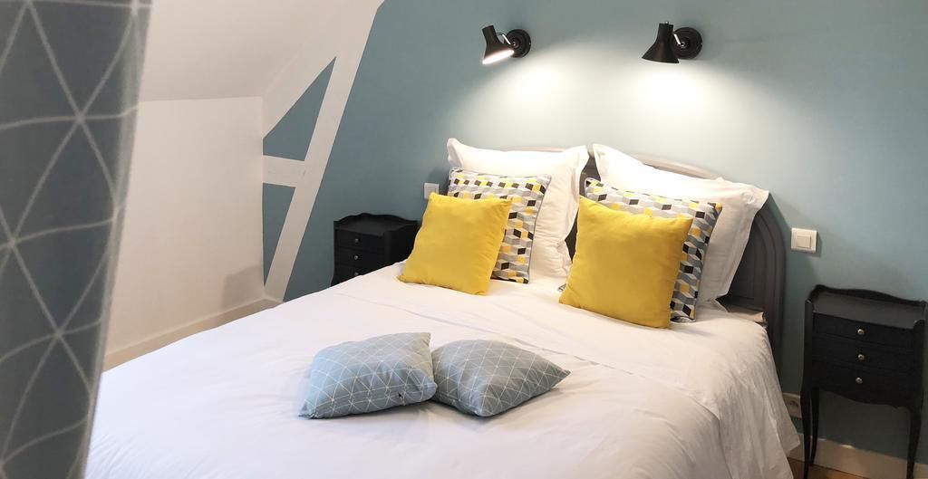 A neatly made bed with white and patterned pillows, a bedside table, and two wall-mounted lamps.