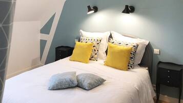 A neatly made bed with white and patterned pillows, a bedside table, and two wall-mounted lamps.