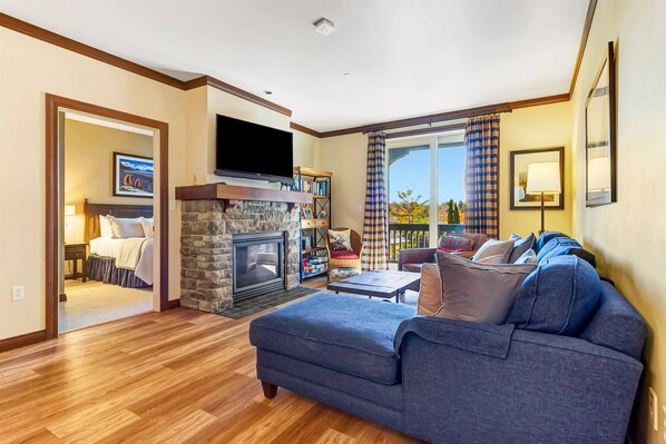 A living room with a stone fireplace, a flat-screen TV, a sofa, and a view of the outdoors.