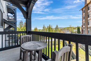 A balcony with a wooden table and chairs, overlooking a landscaped area with trees and a distant view of buildings.