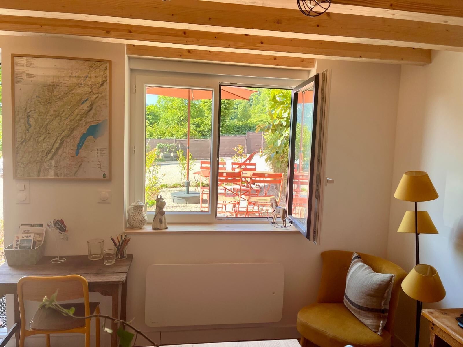 Une pièce avec une grande fenêtre, une carte accrochée au mur, un radiateur, un bureau avec une chaise et un fauteuil jaune.