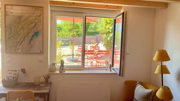 A room with a large window, a map on the wall, a radiator, a desk with a chair, and a yellow armchair.