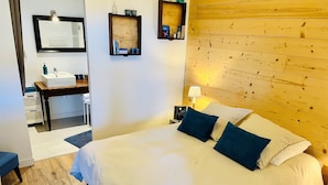 A hotel room with a large bed, a desk with a sink, a mirror, and a wooden headboard. - Gîtes du Fort (Collonges)