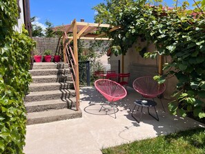 A patio with a wooden pergola, red chairs, and a staircase leading to a covered area. - Gîtes du Fort (Collonges)