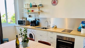 A compact kitchen with a washing machine, a sink, and a dining area with a table and chairs. - Gîtes du Fort (Collonges)