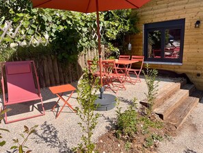 A patio with red furniture, a wooden building, and a gravel ground. - Gîtes du Fort (Collonges)