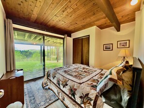 Un dormitorio con una cama grande, techo de madera, puerta corrediza de vidrio a un balcón y una mesita de noche.