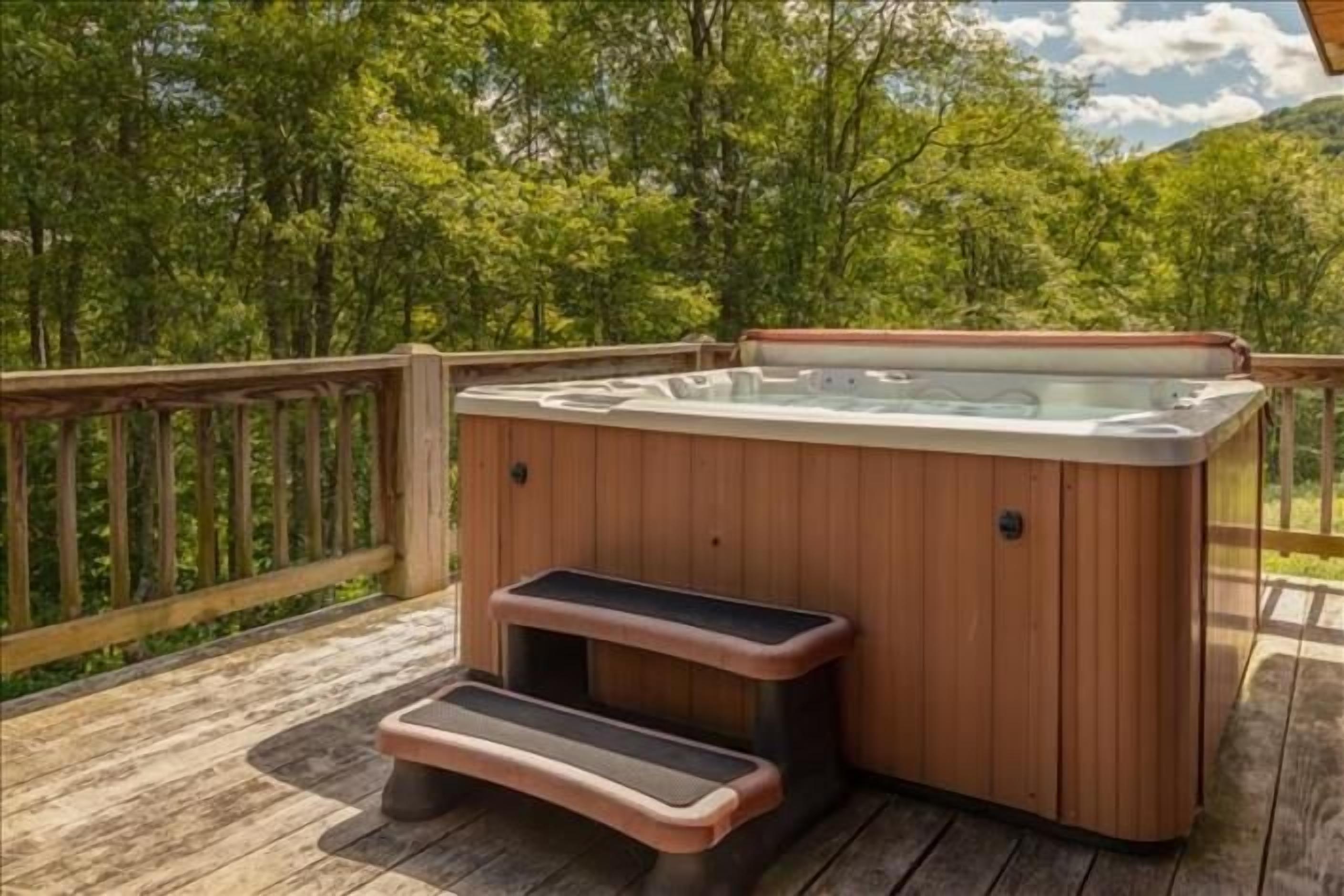 A wooden deck with a hot tub and steps leading up to it, surrounded by trees.