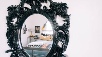 A bedroom with a large ornate mirror, a bed with a striped bedspread, a lamp, and a framed picture on the wall.