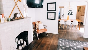 A modern living room with a fireplace, a dining area with a wooden table and chairs, and a TV mounted on the wall. - Designer Historic Duplex Minutes from Downtown (Phoenix)