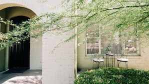 An outdoor seating area with tables and chairs, a brick wall, and a window with shutters. - Designer Historic Duplex Minutes from Downtown (Phoenix)