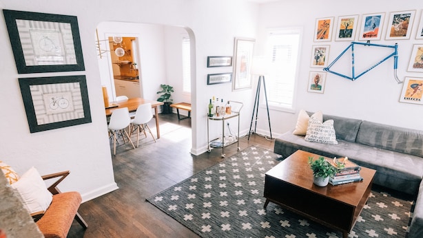 A modern living room with a sofa, coffee table, and a patterned rug. There are framed pictures on the walls and a bicycle in the background. - Designer Historic Duplex Minutes from Downtown (Phoenix)