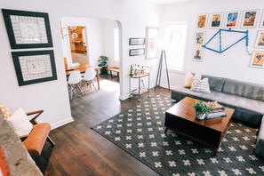 A modern living room with a sofa, coffee table, and a patterned rug. There are framed pictures on the walls and a bicycle in the background. - Designer Historic Duplex Minutes from Downtown (Phoenix)