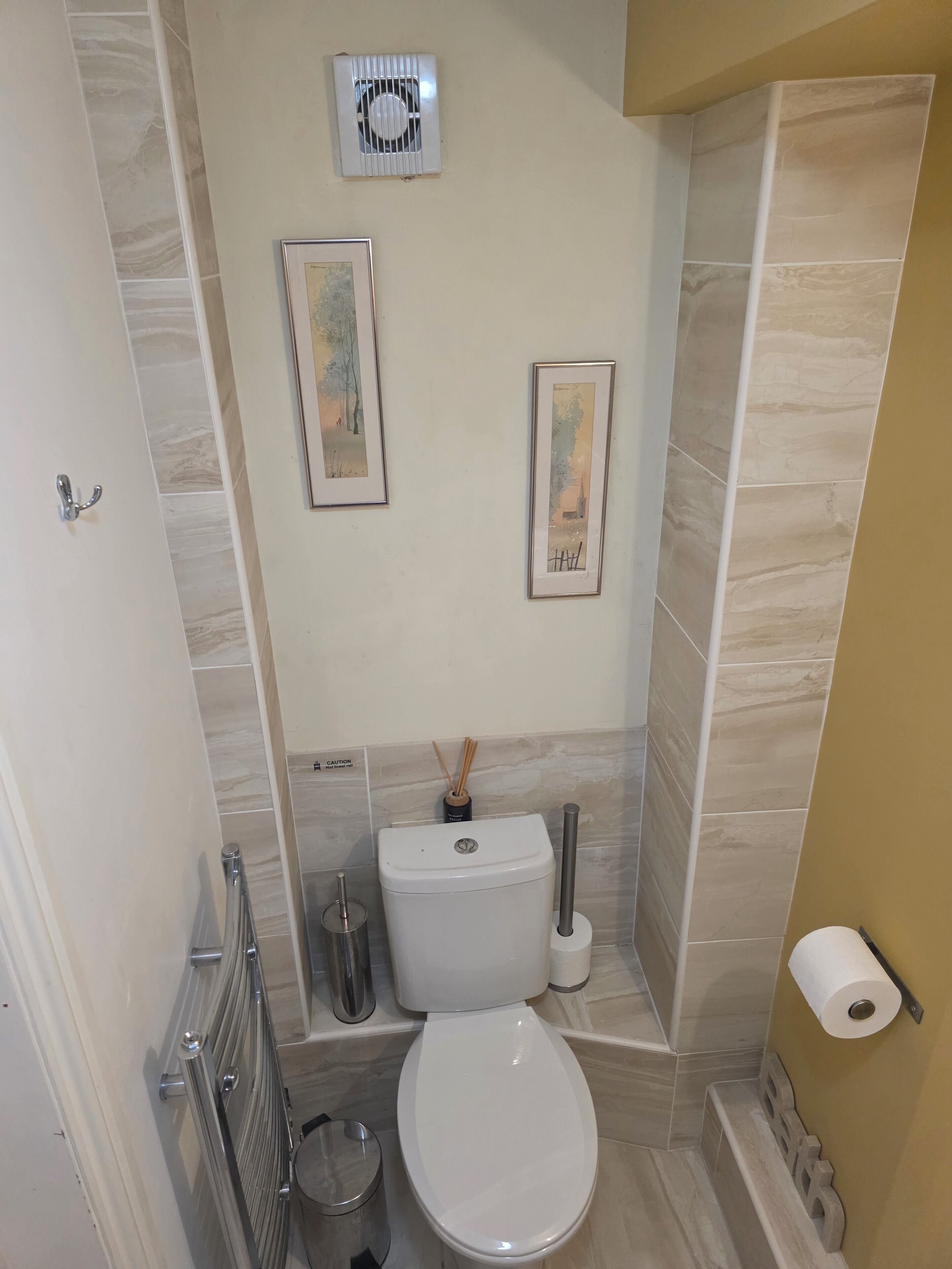 Un baño pequeño con inodoro, radiador, un cuadro enmarcado y una señal de precaución.