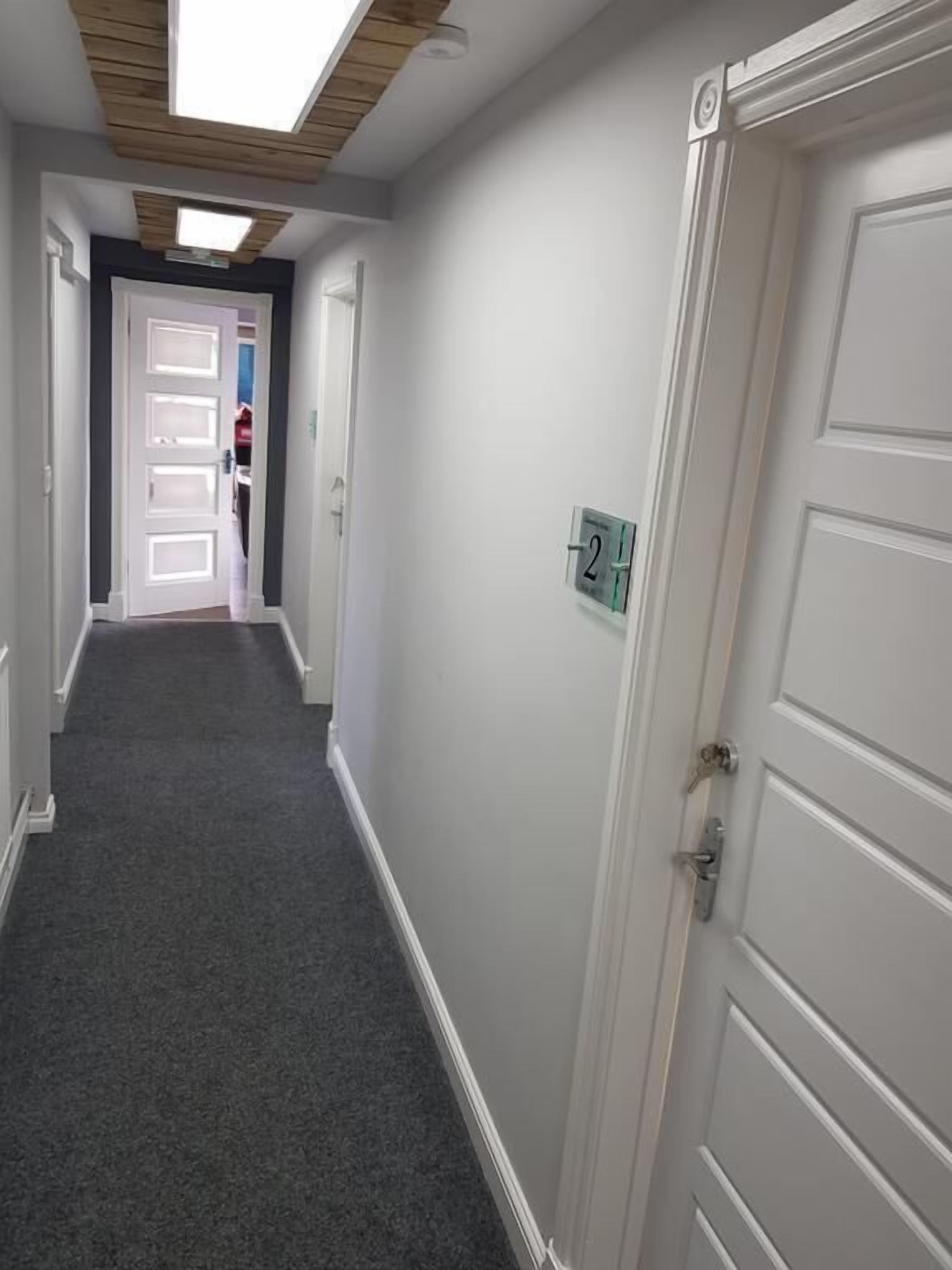 A hallway with a carpeted floor, white doors, and a ceiling with wooden beams and recessed lighting.