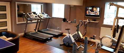A home gym with treadmills, an elliptical, a rowing machine, and a small table.