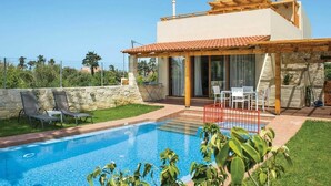Una casa moderna con piscina, zona de estar exterior y un muro de piedra.