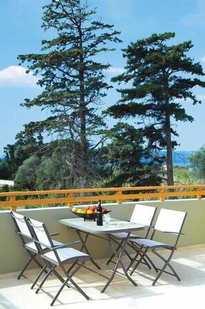 An outdoor patio with a table and chairs, overlooking a scenic landscape with trees and a view of the sea. - Villa Lemonia (Platanias)