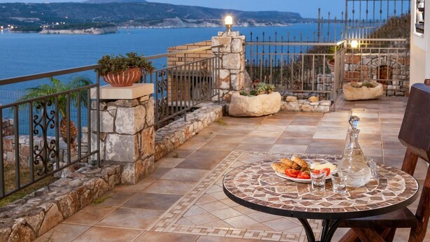 A terrace with a table set for dining, overlooking a coastal view with a mountain in the distance. - Villa Thalassea (Chania)