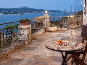Una terraza con una mesa lista para comer, con vista al mar y una montaña al fondo.