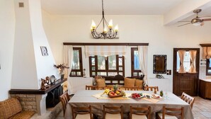 A dining room with a large table, wooden chairs, a chandelier, and a fireplace. - Villa Thalassea (Chania)