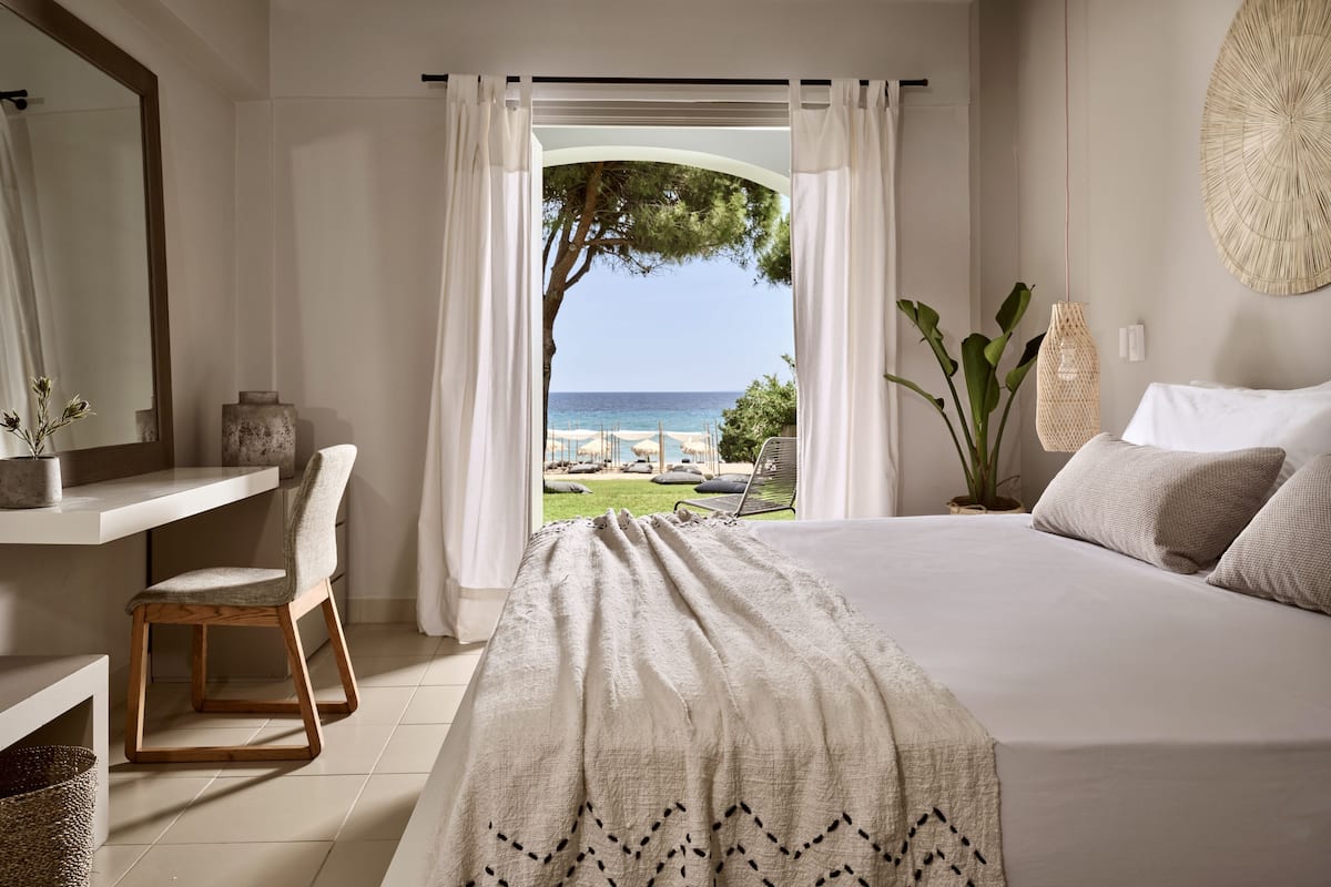 A bedroom with a large bed, a chair, a desk, and a view of the sea.