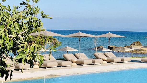 Zona junto a la piscina con sillones de descanso y sombrillas, con vistas a una masa de agua.