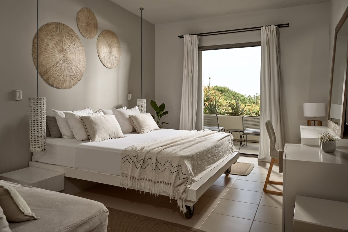 A modern bedroom with a large bed, a desk, and a view of a garden.