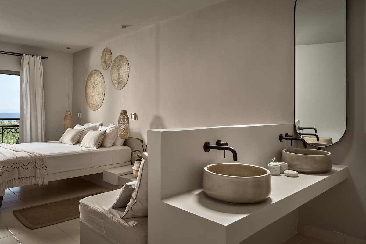 A modern bedroom with a large bed, a bathroom with a round sink and mirror, and a view of the ocean.