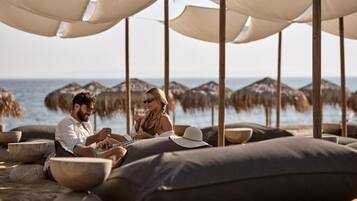 Una pareja sentada en la playa con sombrillas y sillas, con vista al mar.