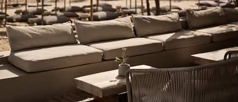 A beachside lounge with a sofa and chairs, umbrellas, and a view of the sea.