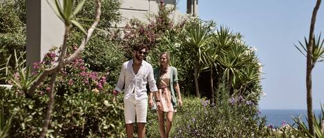 A couple walking on a pathway surrounded by lush greenery and a building with a tiled roof.