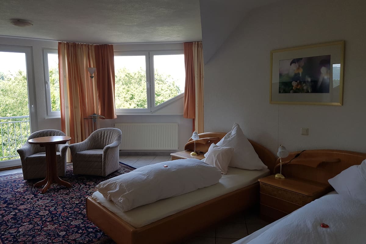 A hotel room with a bed, a chair, a small table, and a window with curtains.